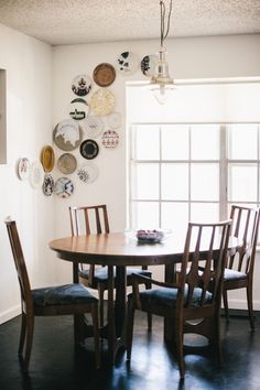 a dining room table and chairs with plates on the wall above it, in front of a window