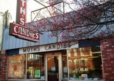 a store front with red flowers in the window and sign above it that says nuts candies