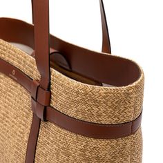 a brown and tan straw bag with leather straps on the bottom, side view in close up