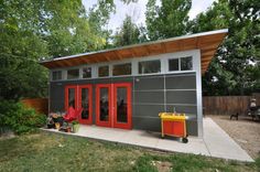 a small gray and red house with two doors on the outside, surrounded by trees