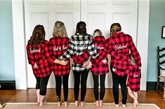 four women in red and black flannel shirts are standing on a door mat