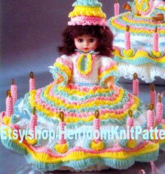 a crocheted cake with candles and a doll sitting on top of it in front of the cake