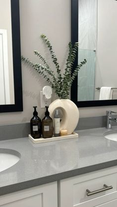 a bathroom with two sinks and a large mirror on the wall above it is a plant in a vase