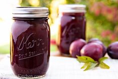 two jars filled with plum jam sitting on top of a table next to some fruit