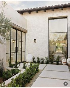 a white stucco house with large windows and plants