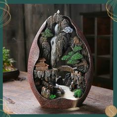 an egg shaped sculpture with a waterfall in the middle and trees around it on a table