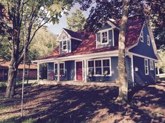 a blue house with red shingles and white trim on the front door is surrounded by trees