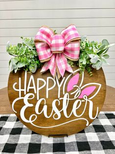 a wooden sign that says happy easter with a pink bow on it and some green plants