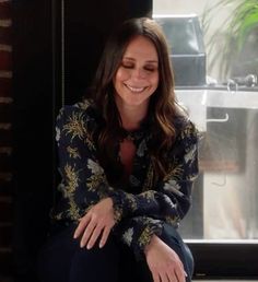 a smiling woman sitting on the ground in front of a window