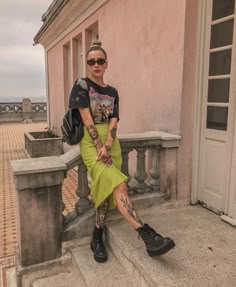 a woman sitting on some steps in front of a pink building with her legs crossed