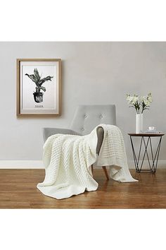 a chair with a blanket on it next to a table and flowers in a vase