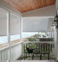 a porch with white blinds and a bench on the front porch overlooking the beach in the background