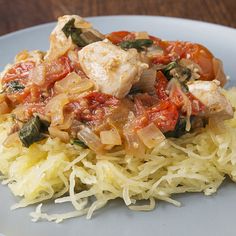 a white plate topped with meat and vegetables on top of spaghetti noodles covered in sauce