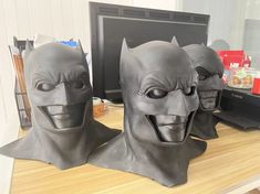 three plastic batman masks sitting on top of a wooden desk next to a computer monitor