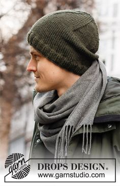 a man wearing a beanie and scarf on the street with trees in the background