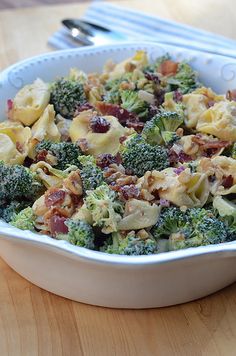 a bowl filled with broccoli, pasta and other food on top of a wooden table