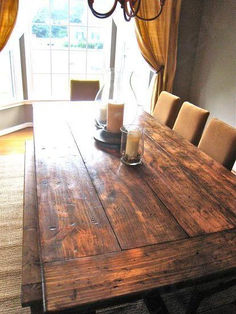 a wooden table with two candles on it in front of a window and some curtains