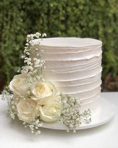 a white wedding cake with flowers on the side and greenery in the back ground