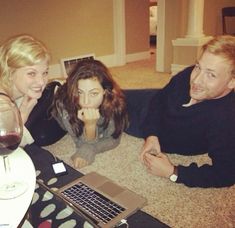 three people sitting on the floor with a laptop and wine glass in front of them