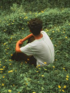 a young man sitting in the middle of a field with yellow flowers on his knees