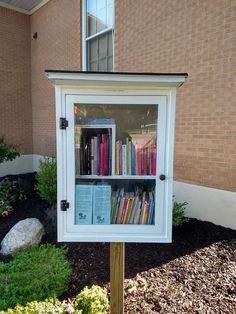 a white book case sitting in front of a brick building filled with lots of books