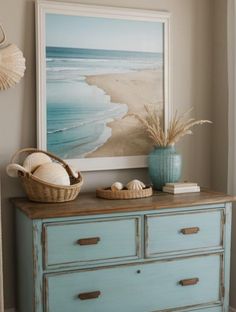 a blue dresser with two baskets on top of it next to a painting and seashells