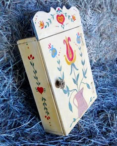 an old wooden box with painted designs on it sitting in the grass and straws