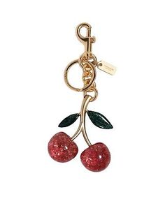 a pair of cherries hanging from a gold plated keychain on a white background