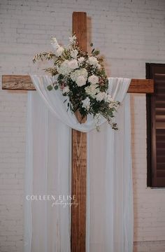 a cross decorated with flowers and greenery in front of a white brick church wall