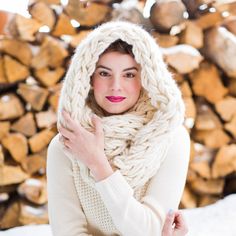 a woman wearing a knitted scarf and posing in front of firewood log pile