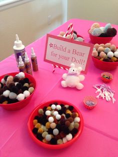 a pink table topped with red bowls filled with candies and teddy bears next to a sign that says build a bear for your doll