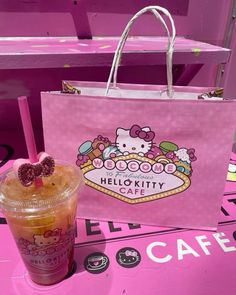 a hello kitty cafe bag next to a drink on a pink table with the hello kitty cafe logo