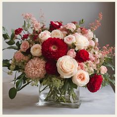 a vase filled with red and white flowers on top of a table next to greenery