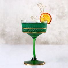 a green glass filled with an orange slice and garnished with sprigs