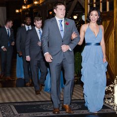 a man and woman in formal wear walking down the aisle at a wedding reception with other people behind them