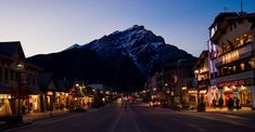 a street lined with shops and buildings in front of a snow covered mountain at dusk