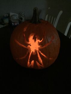 a carved pumpkin with the shape of a spider on it's face, sitting on a table