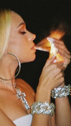 a woman in a white dress holding a lit candle up to her mouth while wearing bracelets