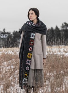 a woman standing in the snow wearing a black scarf with colorful flowers and crochet