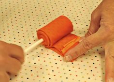 two hands are holding an orange piece of cloth on top of a polka dot tablecloth