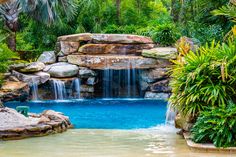 an outdoor pool with waterfall and tropical plants surrounding it, surrounded by trees and shrubs