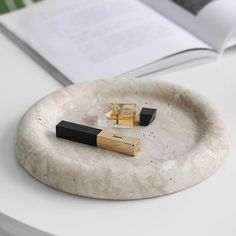 an open book on a table next to two small black and gold objects in a marble plate