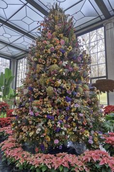 a very tall christmas tree surrounded by lots of flowers