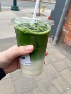 a person holding up a drink with green liquid