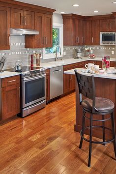 a large kitchen with wooden floors and stainless steel appliances, along with white counter tops