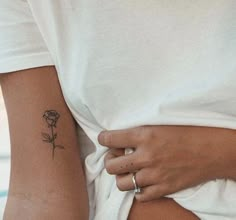 a woman with a small rose tattoo on her left arm and the other hand behind her back