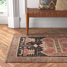 a wooden bench sitting on top of a hard wood floor next to a rug and pillows