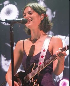 a woman singing into a microphone while holding a guitar in front of her face and smiling