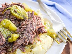 a white plate topped with mashed potatoes covered in beef and pickles next to a fork