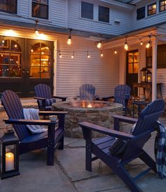 an outdoor fire pit with chairs around it and lights on the side of the building